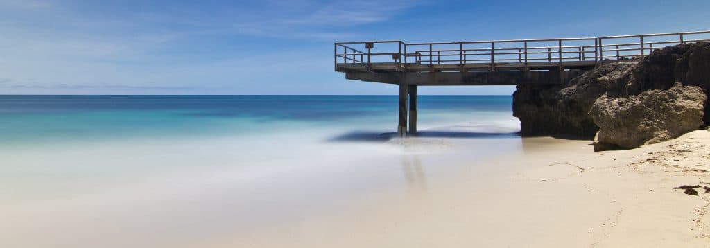 Calm beach with a rocky jetty under clear sky.