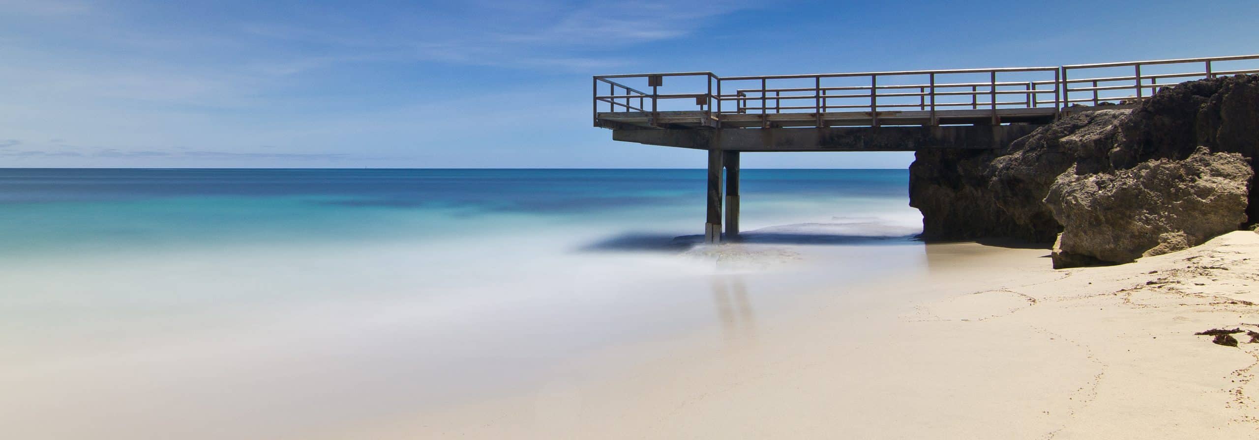 Calm beach with a rocky jetty under clear sky.